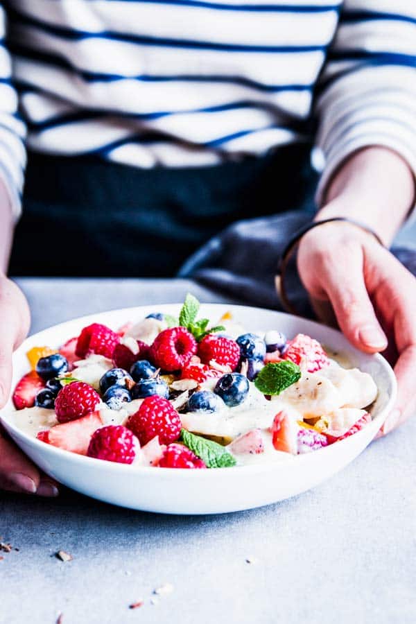 Woman in a striped t-shirt serving creamy fruit salad.