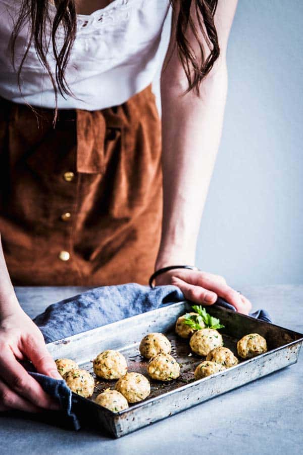 Woman serving a tray of baked Greek Turkey Meatballs.