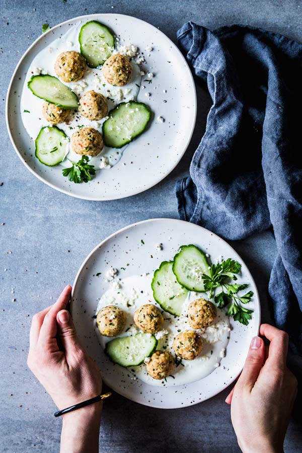 Two white plates with greek turkey meatballs, cucumber and yogurt. Black napkin.