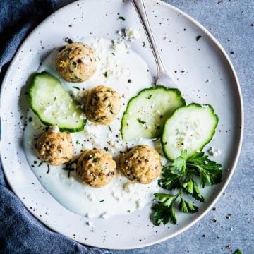 Greek Turkey Meatballs with cucumber and yogurt sauce on a white plate. With a fork and a black napkin.