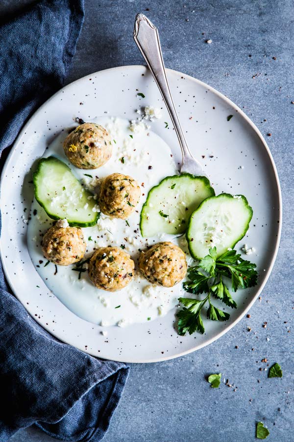 Greek Turkey Meatballs with cucumber and yogurt sauce on a white plate. With a fork and a black napkin.