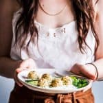 Woman in a white top and tan skirt holding a plate of greek turkey meatballs.