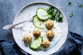 Greek turkey meatballs on a white plate with yogurt, cucumber slices and a fork. Black napkin next to it.