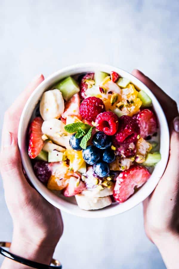 Holding a white bowl with Greek Yogurt Fruit Salad.