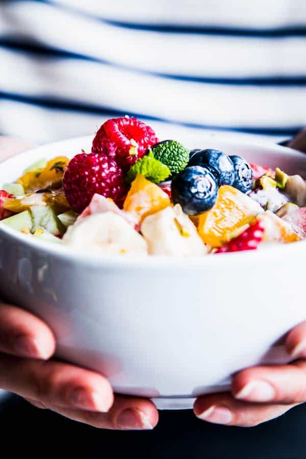 Woman in a striped shirt holding a bowl of Greek Yogurt Fruit Salad.