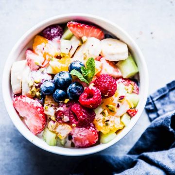 Greek Yogurt Fruit Salad in a white bowl with mint and a dark napkin.