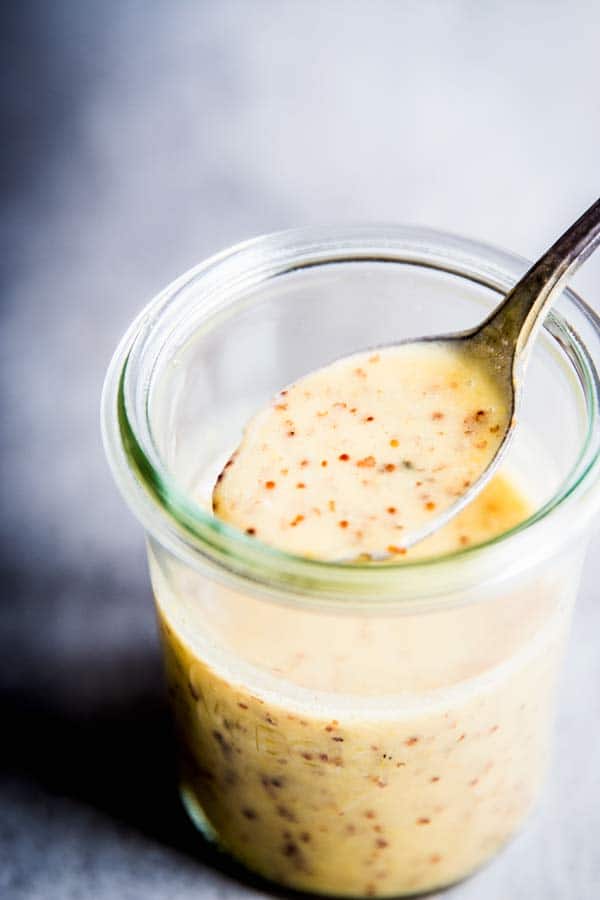 Spooning Honey Mustard Salad Dressing out of a glass jar.