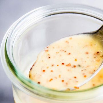 Spooning Honey Mustard Salad Dressing from a glass jar.
