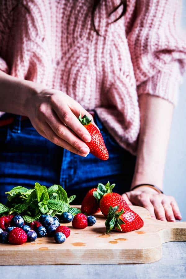 Woman in a pink sweater holding a strawberry.