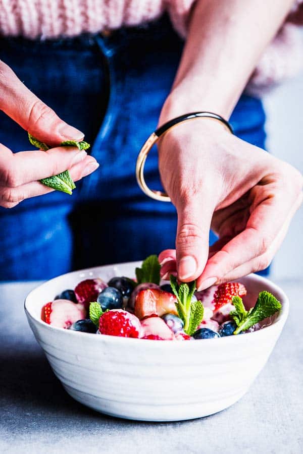Woman adding fresh mint to a bowl of fruit salad.