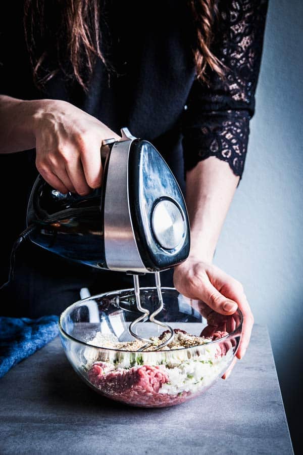 Woman mixing meat, herbs and aromatics to make homemade meatballs.