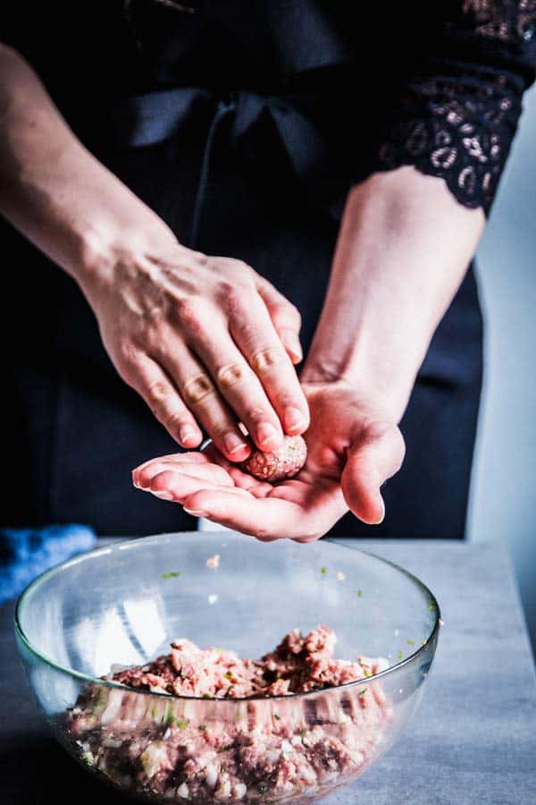 Woman in a black jumpsuit, making homemade meatballs.