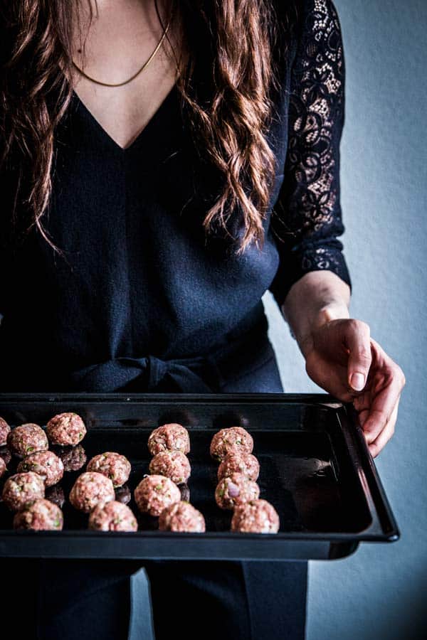 Woman in a black jumpsuit, holding a sheet pan full of homemade meatballs.