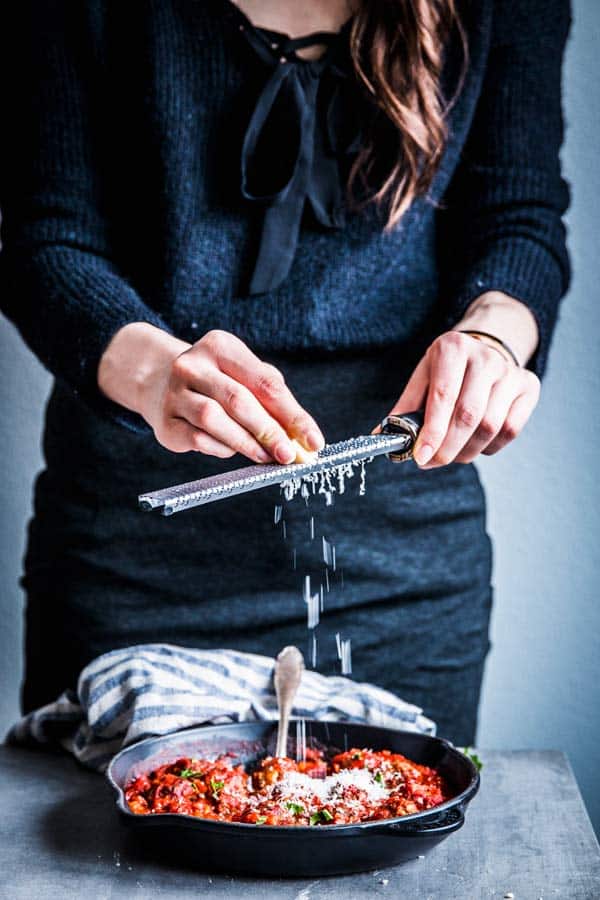 Woman in a black dress grating parmesan on top of Italian meatballs.