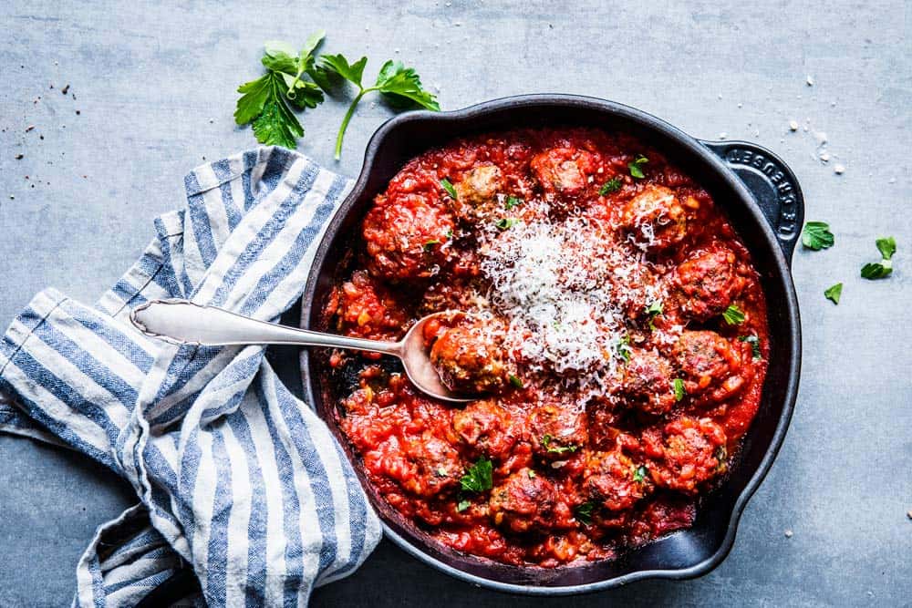 Photo of easy Italian meatballs in a black cast iron skillet with a spoon.