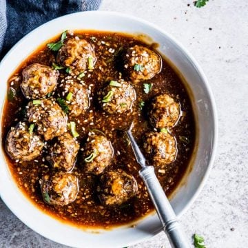 Korean BBQ Meatballs in a white bowl with a spoon and black napkin.