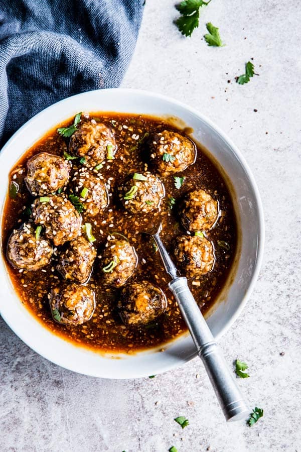 Korean BBQ Meatballs in a white bowl with a spoon and black napkin.