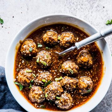 Korean BBQ Meatballs in a white bowl with a spoon, cilantro and black napkins.
