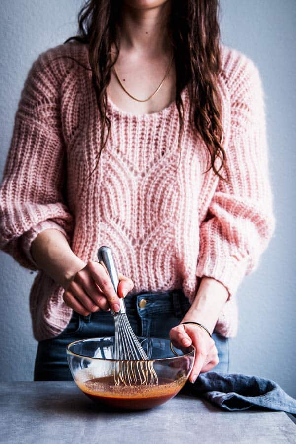 Woman in a pink sweater whisking pineapple bbq sauce.