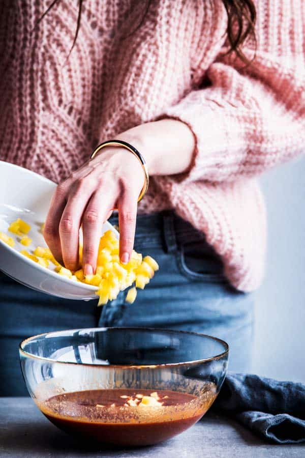 Woman in a pink sweater adding fresh pineapple chunks to pineapple bbq sauce.