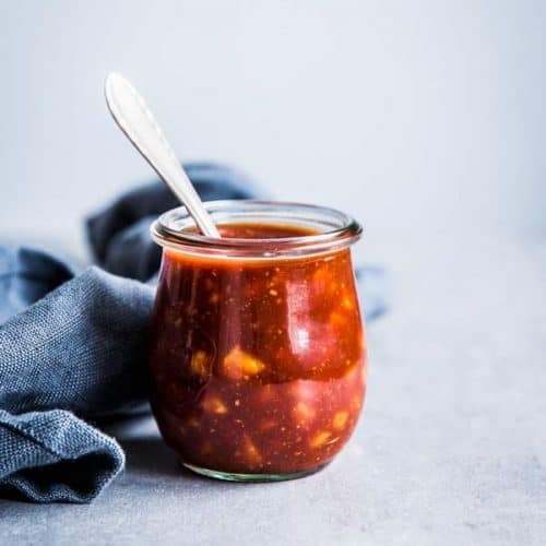 Pineapple BBQ Sauce in a small glass jar with a spoon and a black napkin on the table.