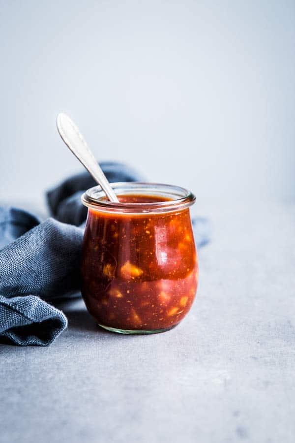 Pineapple BBQ Sauce in a small glass jar with a spoon and a black napkin on the table.