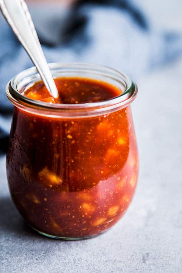 Close up of Pineapple BBQ Sauce in a small glass jar with a spoon.