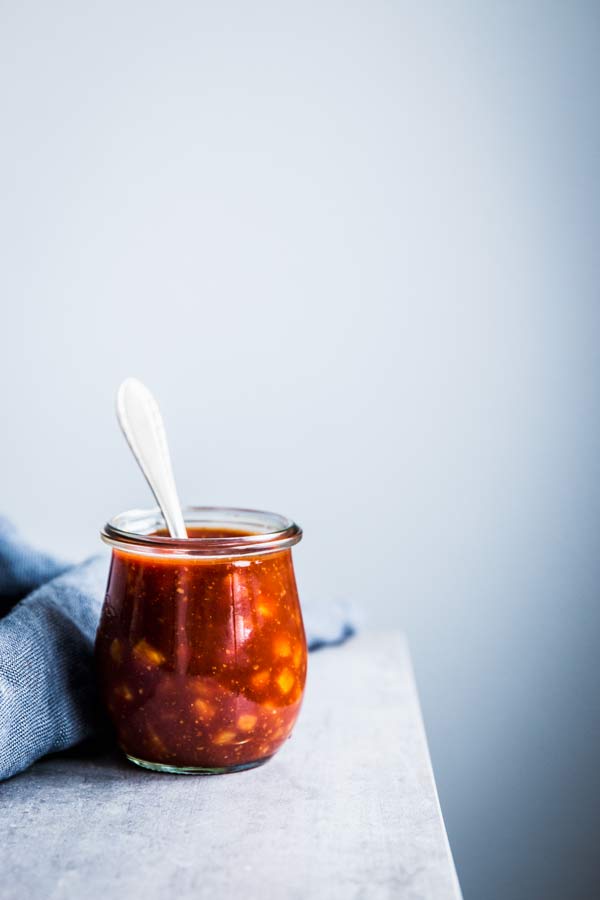 Pineapple BBQ Sauce in a small glass jar with a spoon and a dark napkin on the table.