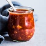 Pineapple BBQ Sauce in a small glass jar with a spoon and a black napkin.