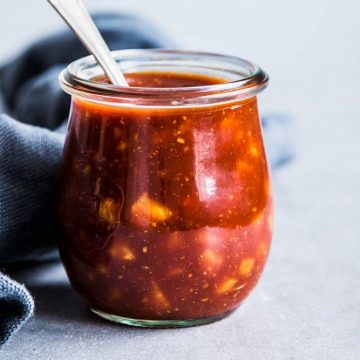 Pineapple BBQ Sauce in a small glass jar with a spoon and a black napkin.