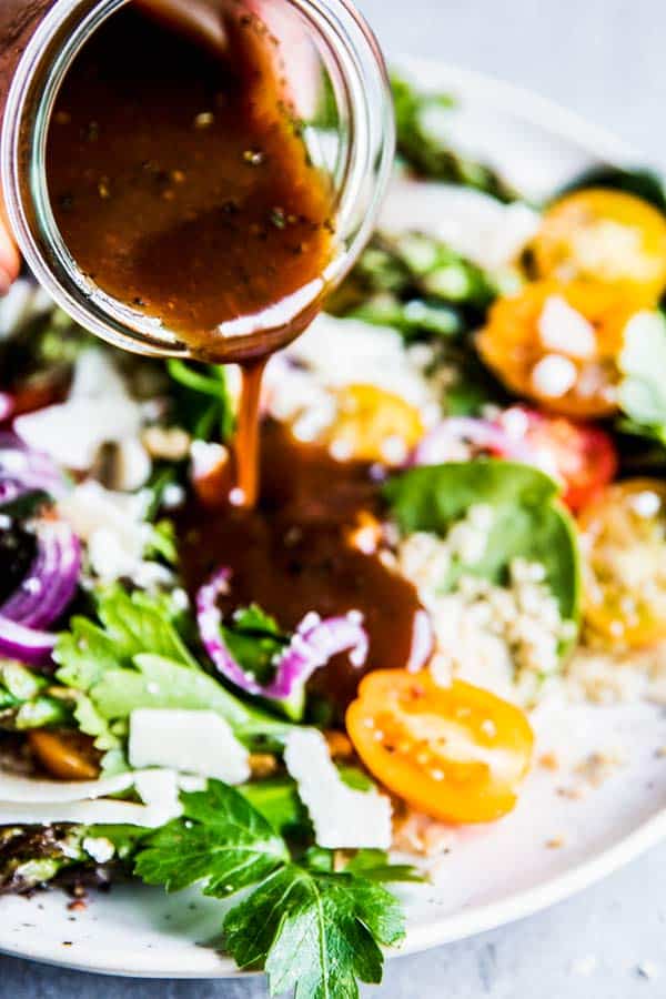 Pouring Spooning Balsamic Vinaigrette Dressing over Quinoa Spinach Salad.