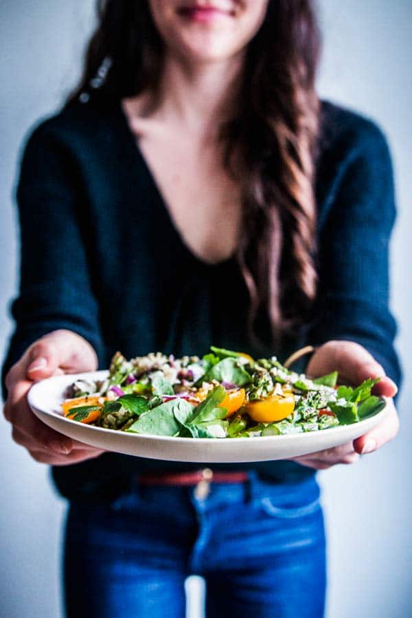 Woman in blue jeans and a black sweater holding a plate of quinoa spinach salad with asparagus.