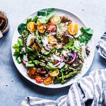 Quinoa Spinach Salad with Asparagus on a white plate with balsamic vinaigrette and a striped linen.