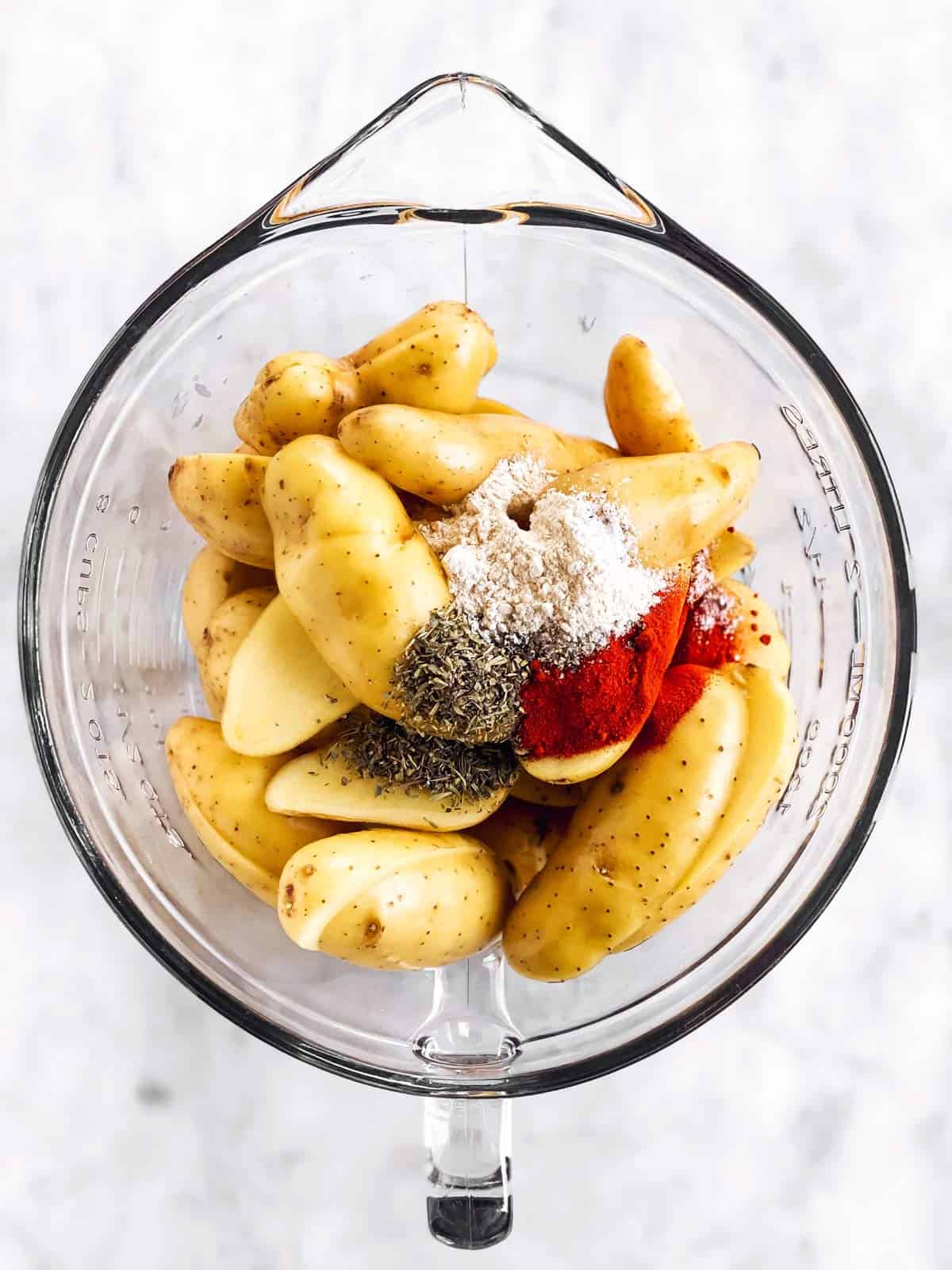 glass bowl filled with halved fingerling potatoes and seasoning