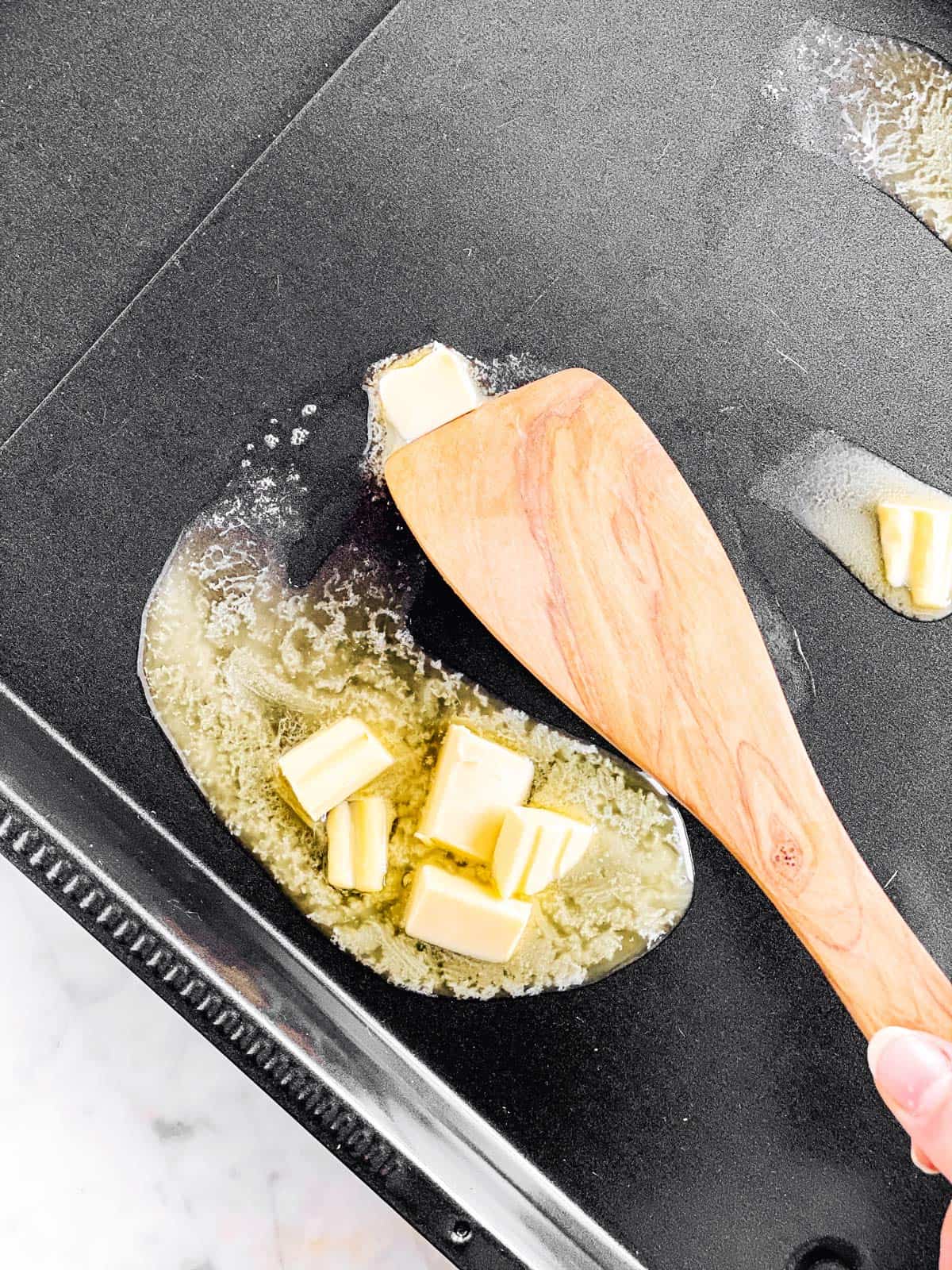 dark pan with melting butter and wooden spoon on top