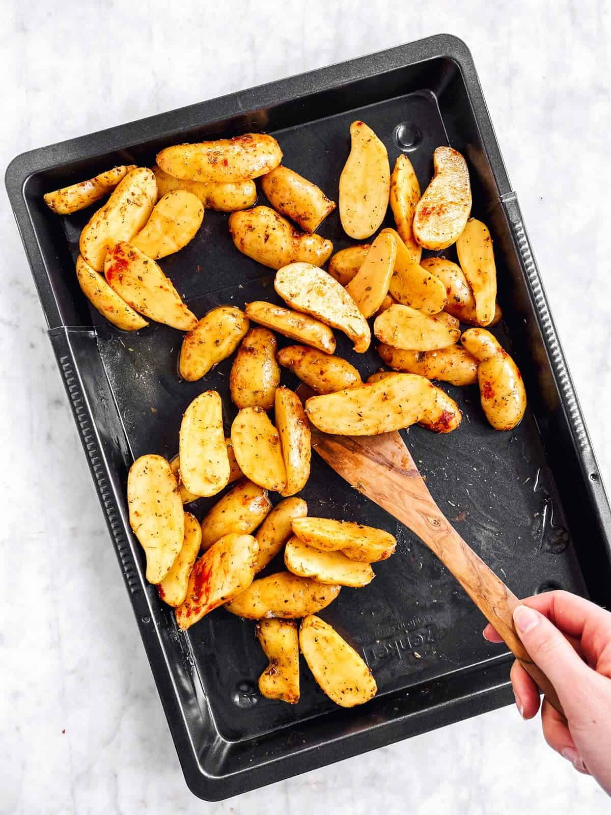 female hand tossing potatoes with wooden spoon on dark pan