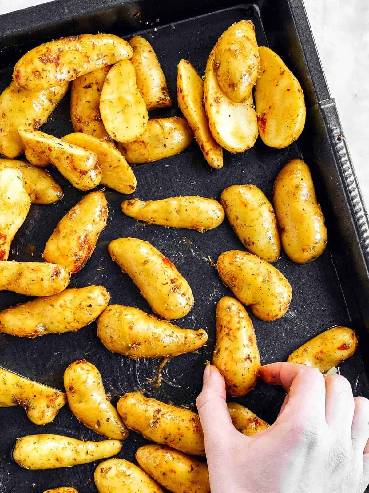 female hand flipping halved fingerling potato on black pan