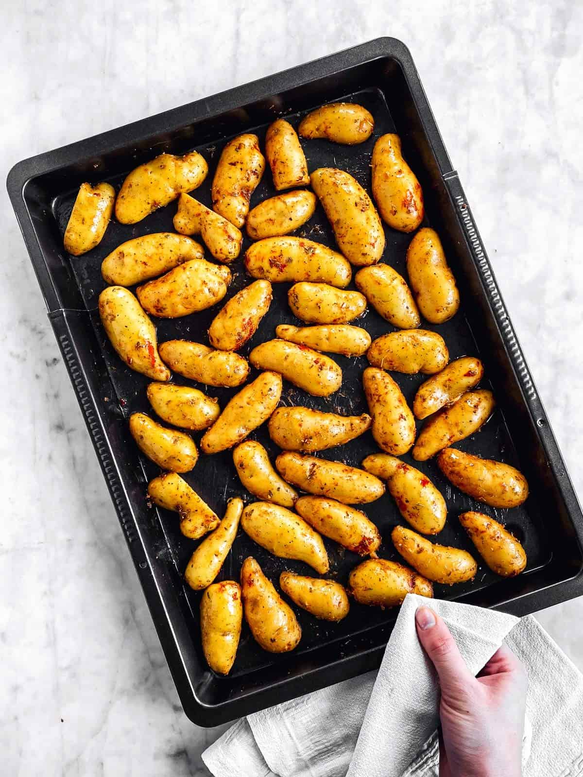 female hand holding dark pan with halved fingerling potatoes