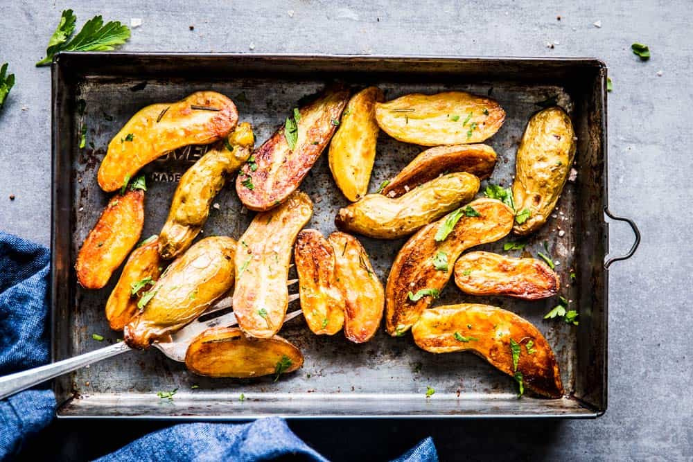 Roasted Fingerling Potatoes on a sheet pan with fresh parsley, next to a blue napkin.