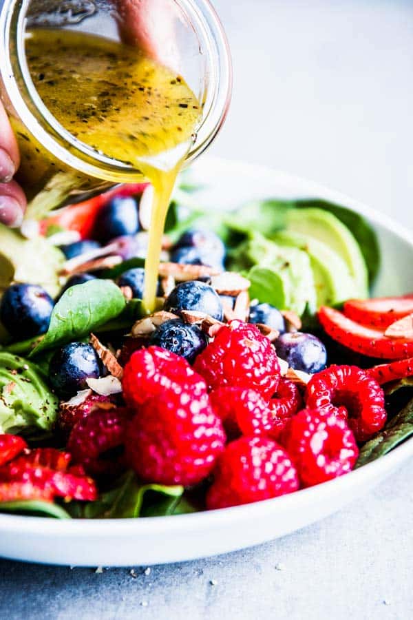 Pouring White Balsamic Vinaigrette over Spinach Avocado Salad.