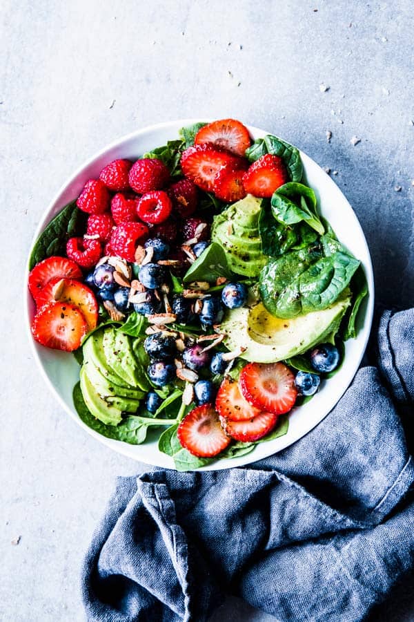 Spinach Avocado Salad in a white bowl with a dark napkin next to it.