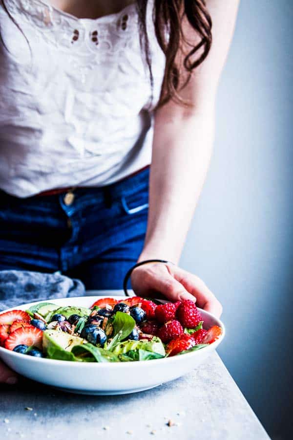 Woman in a white top serving a bowl of Spinach Avocado Salad.