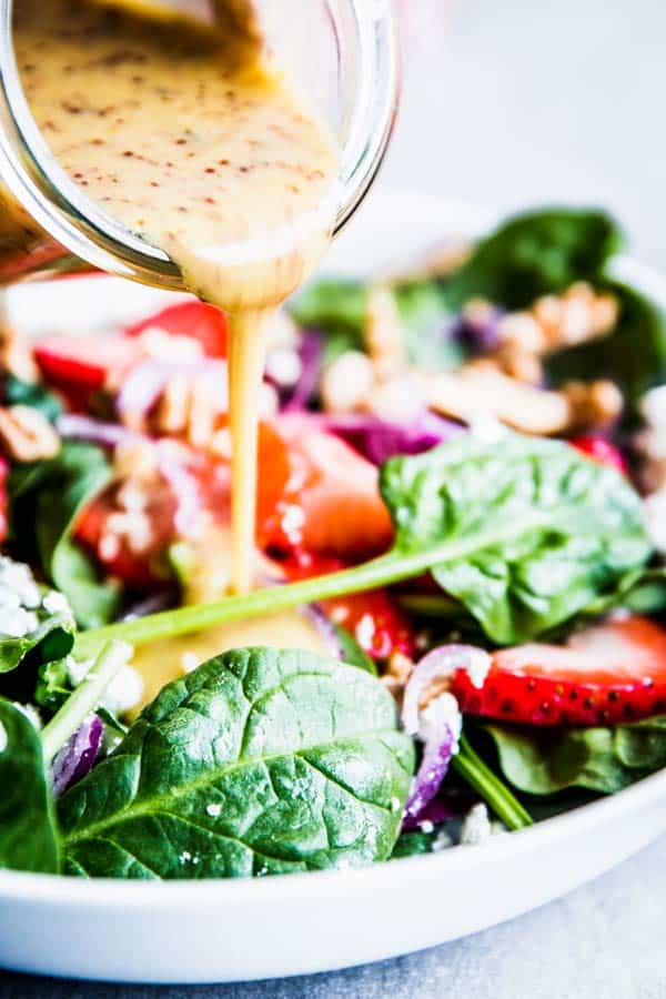 Pouring Honey Mustard Dressing over Spinach Strawberry Walnut Salad