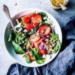 Spinach Strawberry Walnut Salads in a white bowl with a black napkin and a jar of dressing.