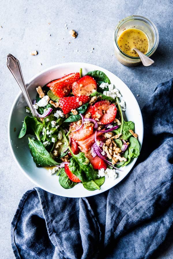 Spinach Strawberry Walnut Salads in a white bowl with a black napkin and a jar of dressing.