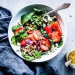 Spinach Strawberry Walnut Salad in a white bowl with dressing on the side.