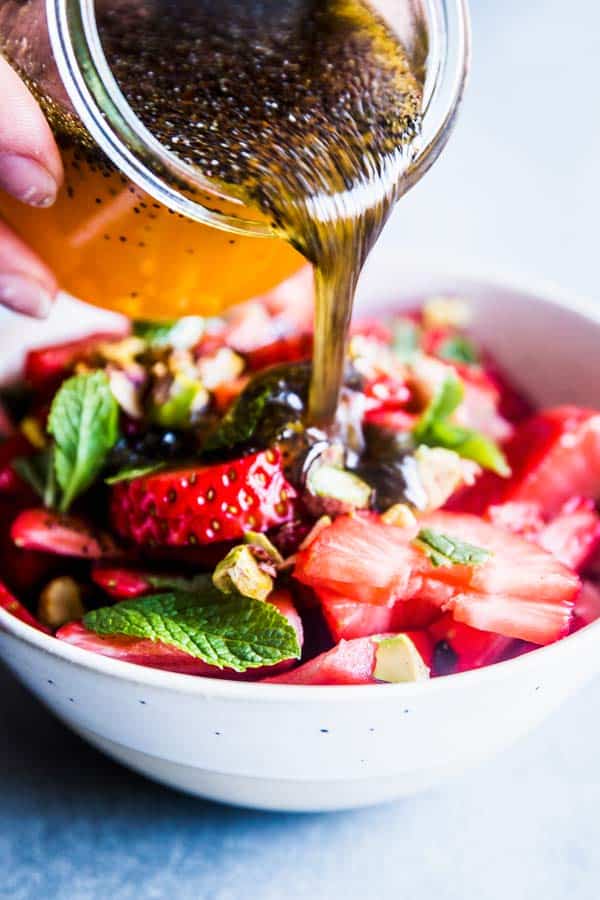 Pouring poppy seed fruit salad dressing over strawberry fruit salad.