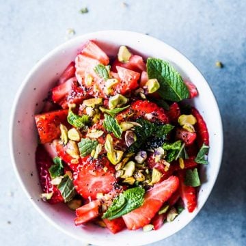 Strawberry Fruit Salad with mint and pistachios in a white bowl.