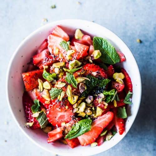 Strawberry Fruit Salad with mint and pistachios in a white bowl.