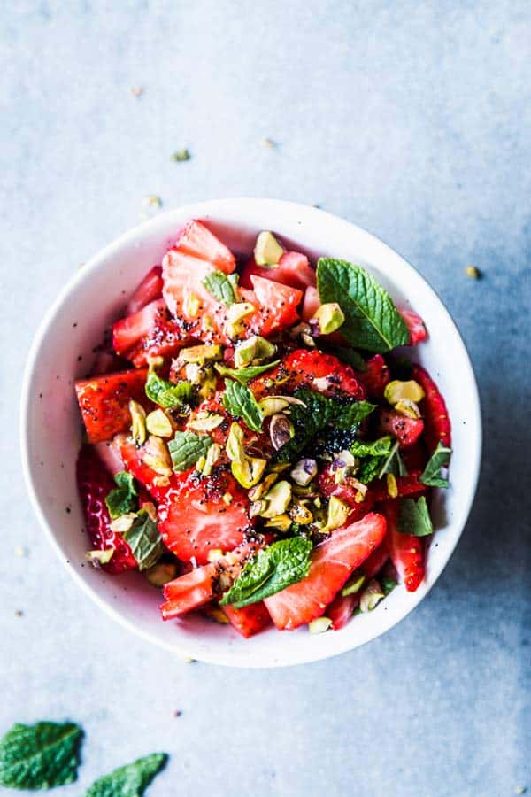 Strawberry Fruit Salad with mint and pistachios in a white bowl.